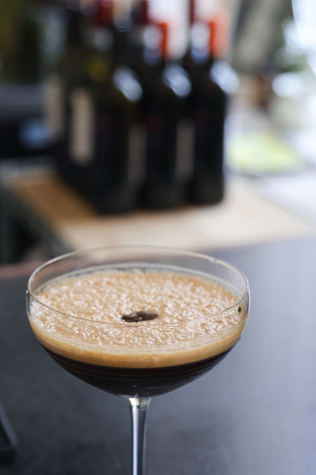 An espresso martini in a coupe glass, blurred bottles behind the bar